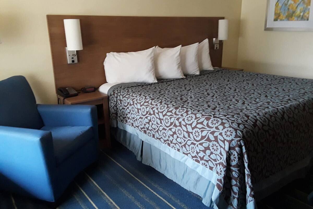 Een hotelkamer met een bed, een stoel, een nachtkastje met een telefoon en een wandlamp.