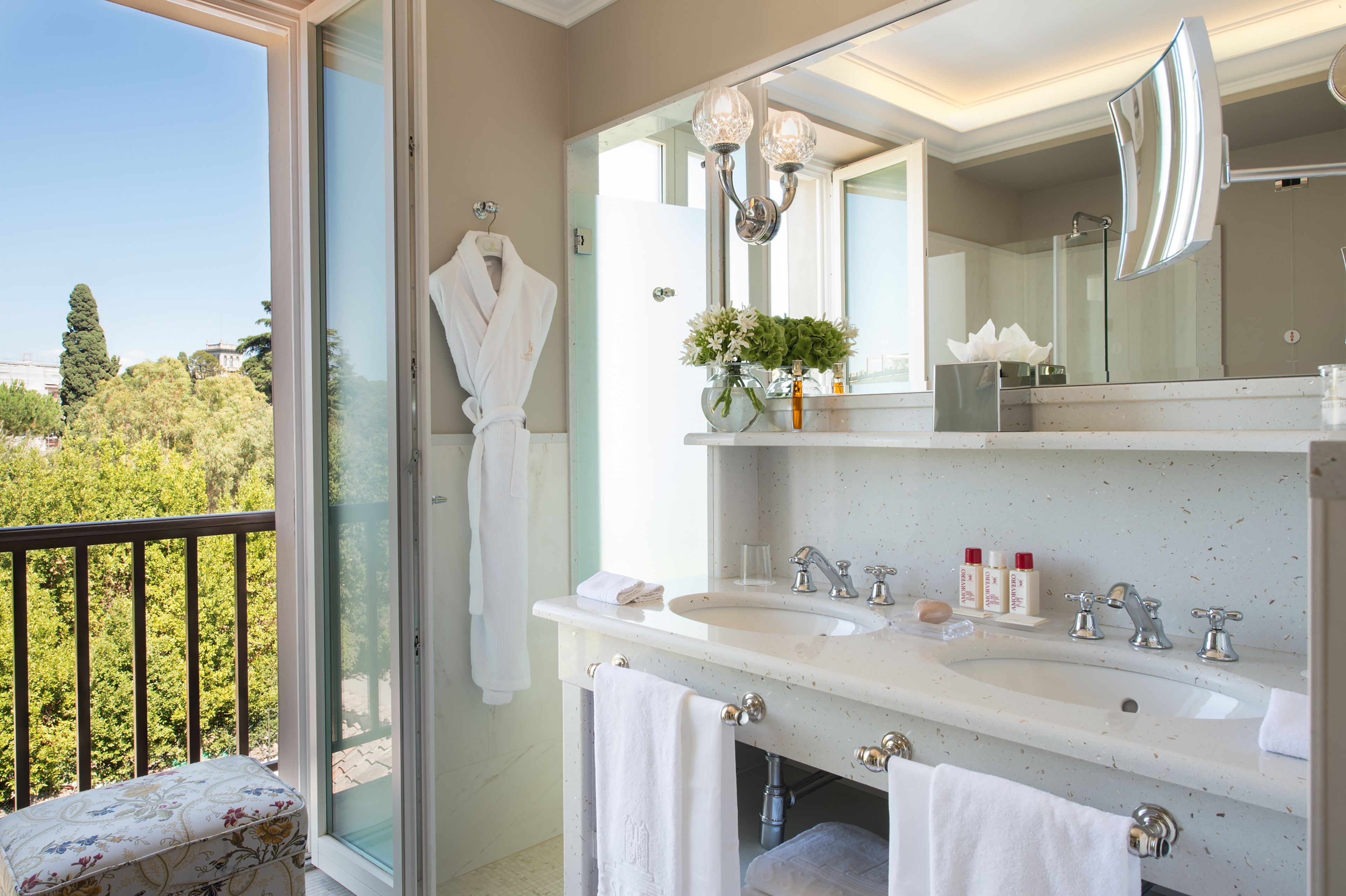 A bathroom with a large window, a white sink, a mirror, and a towel rack.