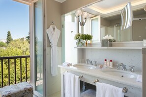 A bathroom with a large window, a white sink, a mirror, and a towel rack.