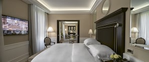 A hotel room with a large bed, a television mounted on the wall, a desk with a lamp, and a mirror.