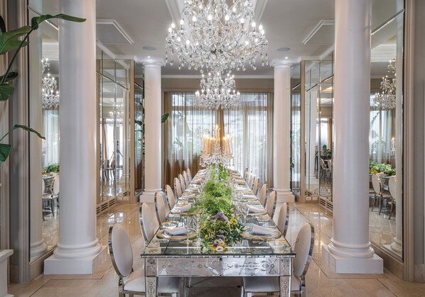 A long dining table set for a formal event, flanked by tall columns, with a large chandelier above. - Hassler Roma (Rome)