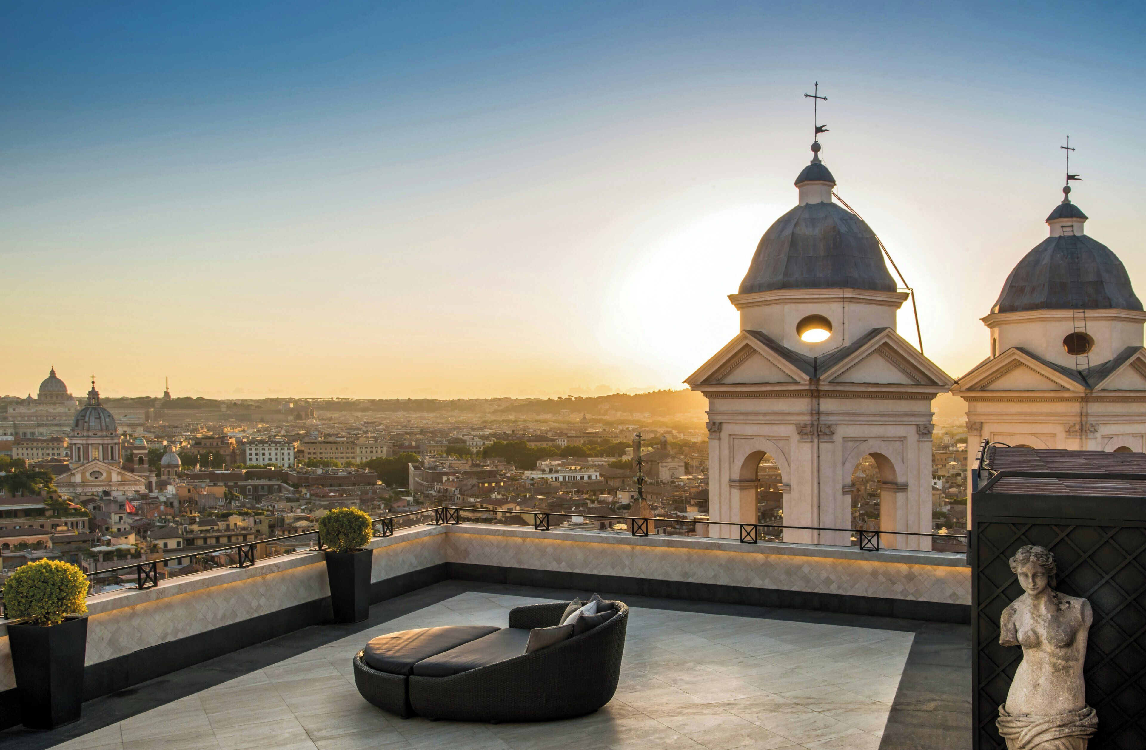 Une terrasse sur le toit, dotée d’un espace salon, d’une statue et offrant une vue sur les bâtiments de la ville et une structure en forme de dôme.