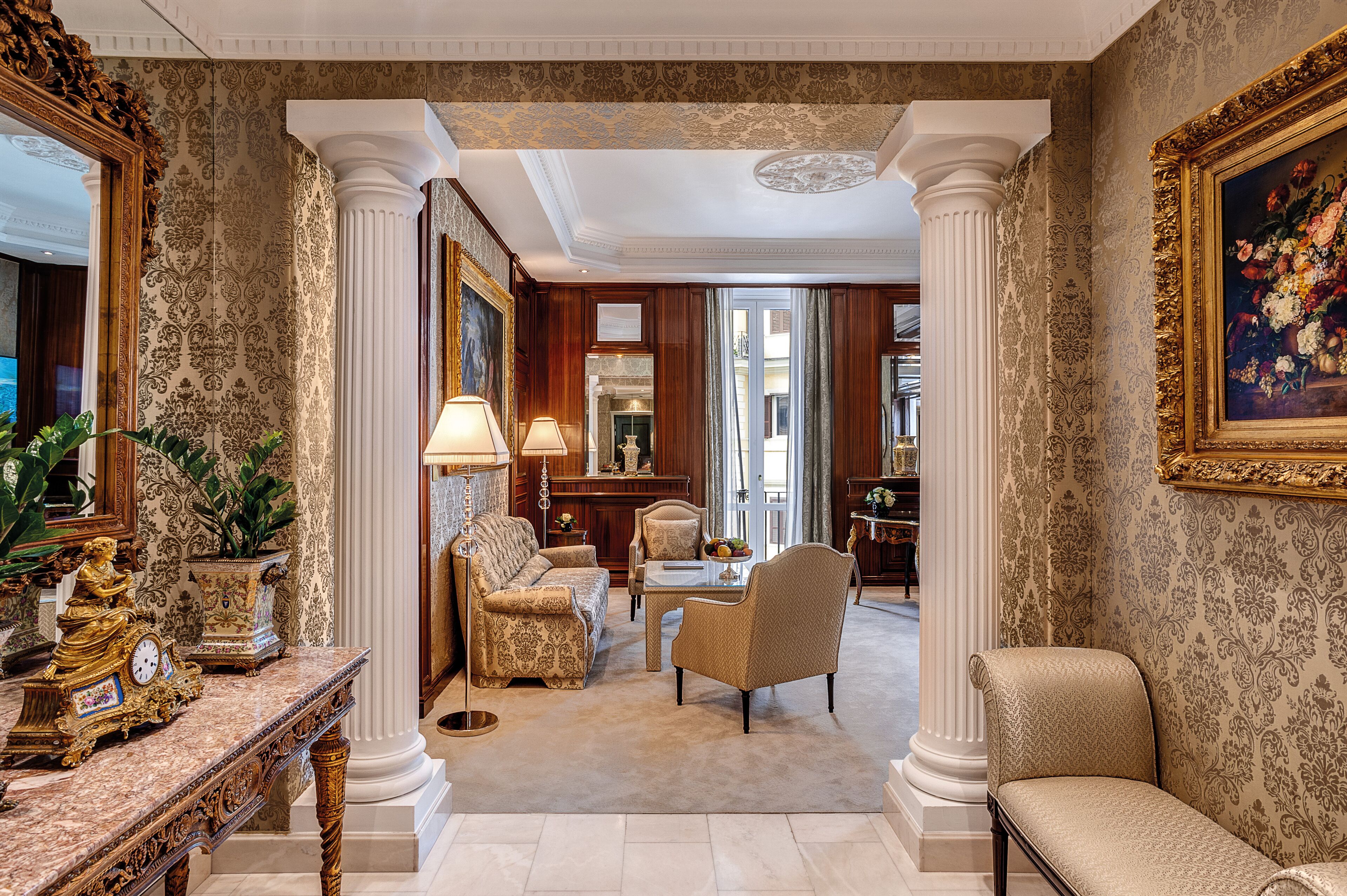 Una sala amplia con papel tapiz decorativo, un espejo grande y muebles clásicos.