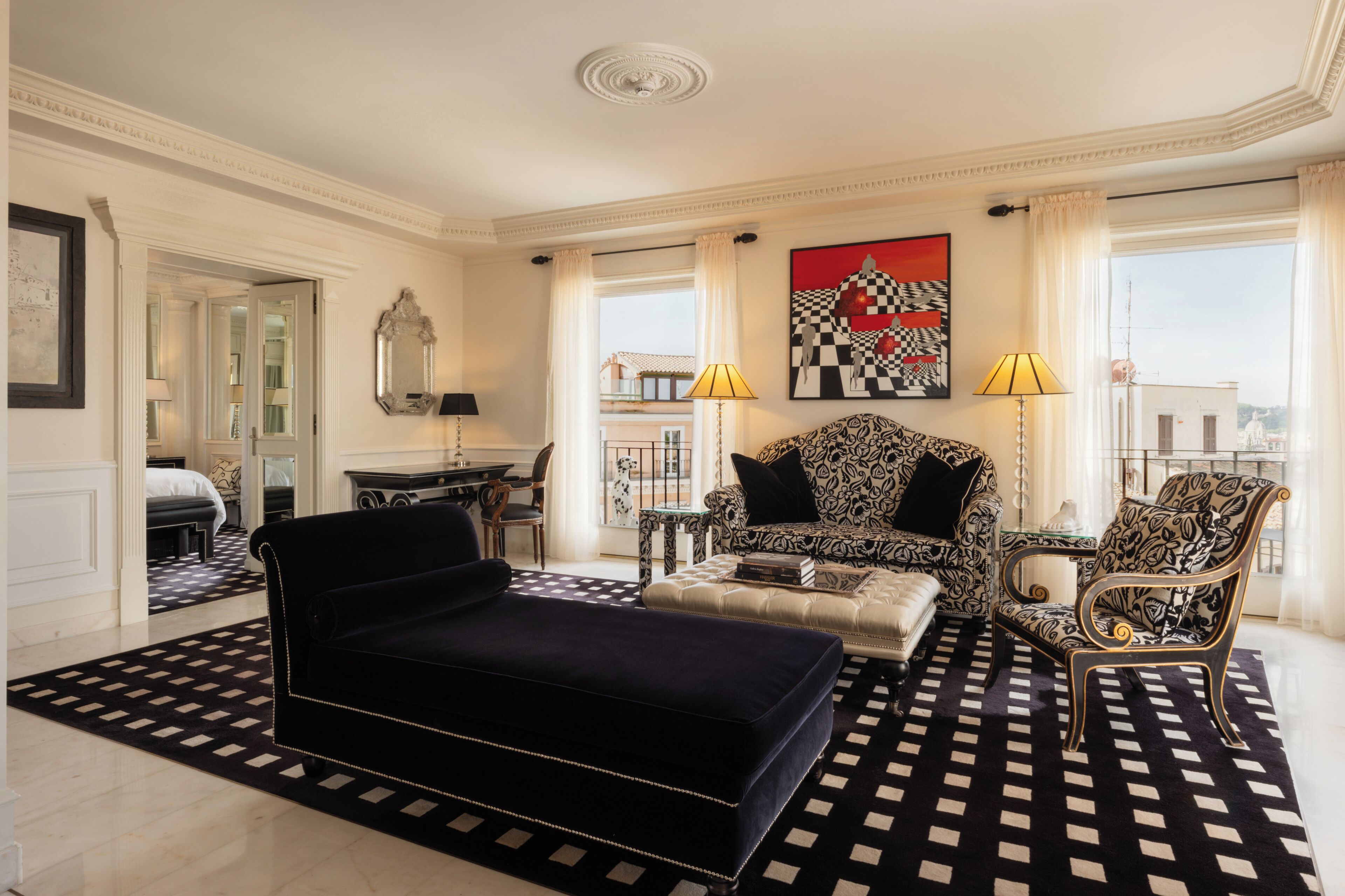 A spacious living room with a black and white patterned rug, a black sofa, a patterned armchair, and a coffee table.