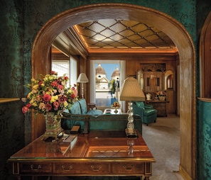 A luxurious room with a wooden desk, a vase of flowers, a lamp, and a view of a building with domes. - Hassler Roma (Rome)