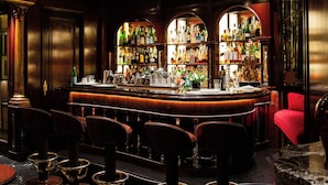 Un bar con suelo de mármol, taburetes y una barra repleta de licores.
