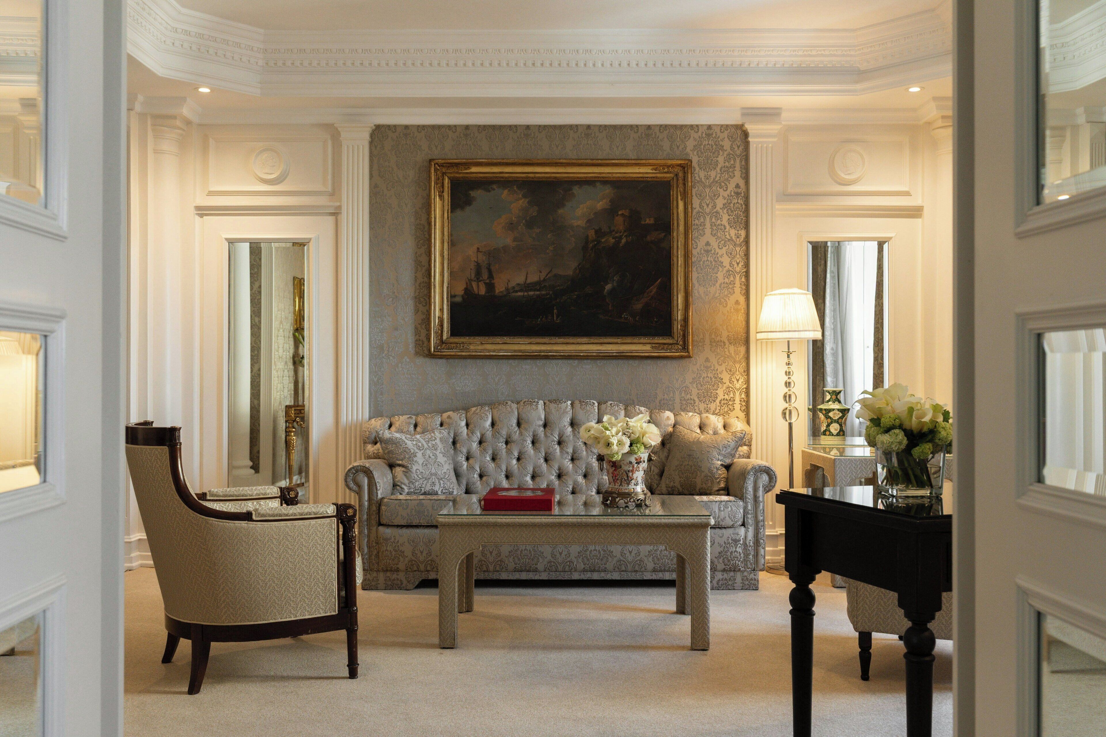 A room with a tufted sofa, a coffee table, a chair, a painting on the wall, and a vase with flowers.