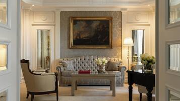 A room with a tufted sofa, a coffee table, a chair, a painting on the wall, and a vase with flowers.