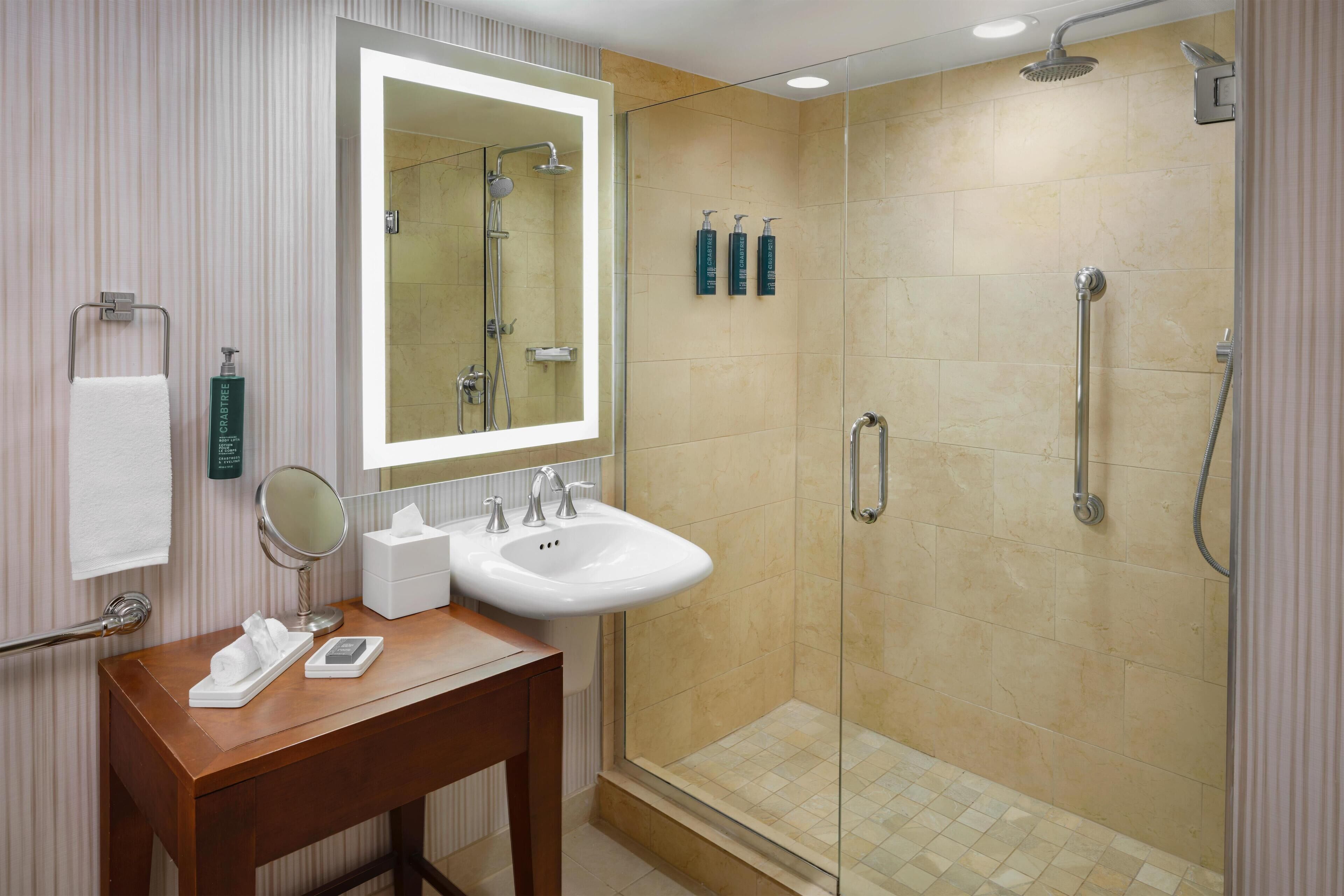 A modern bathroom with a glass-enclosed shower, a vanity with a sink, and a large mirror.