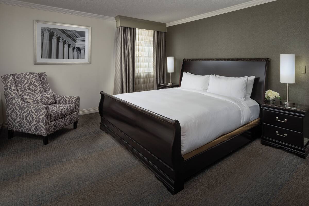 Una habitación de hotel con una cama grande, una silla, una mesita de noche y un cuadro en la pared.
