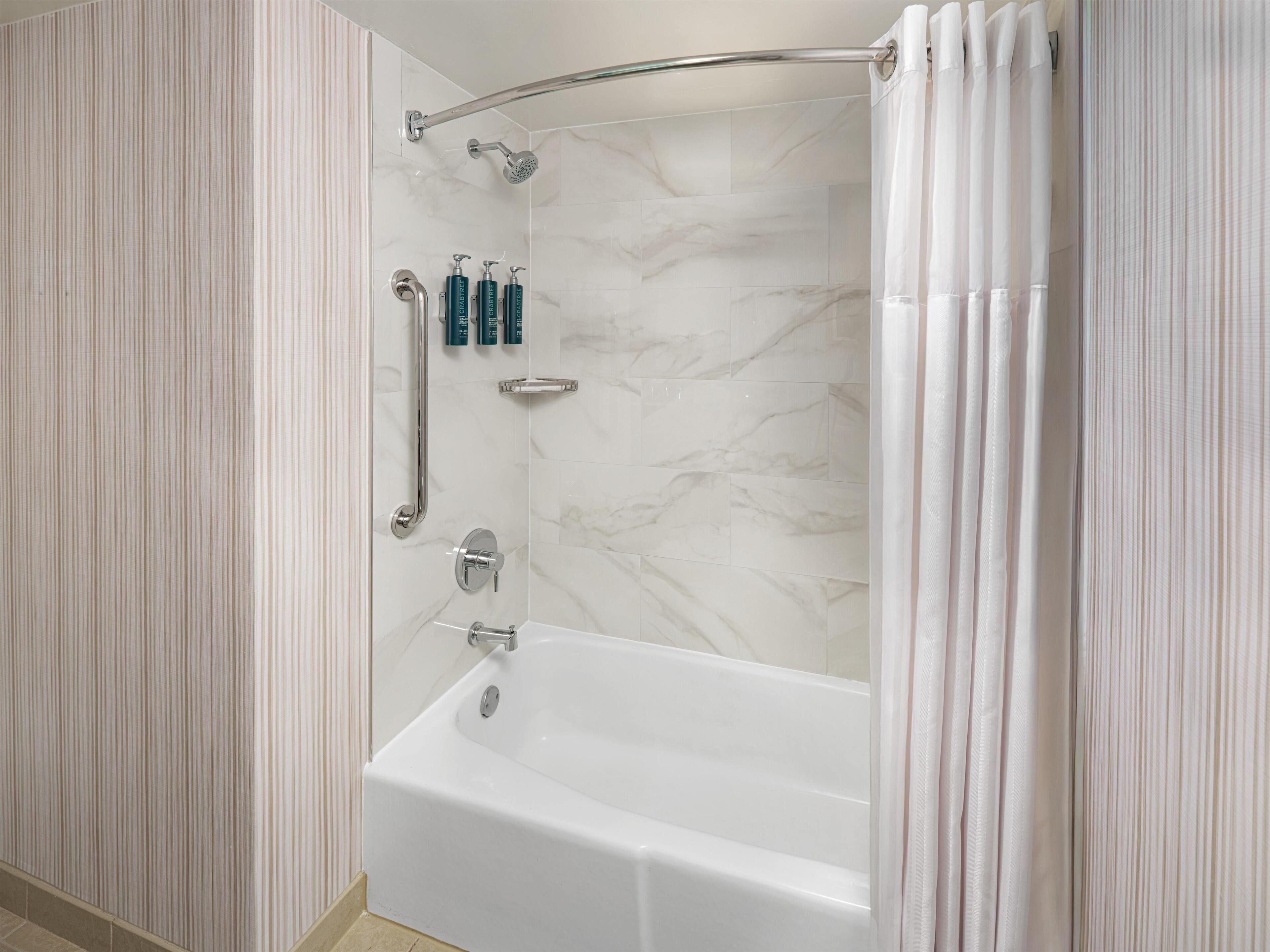 Een moderne badkamer met een marmeren wand, een badkuip, een douche met glazen deur en een handgreep.