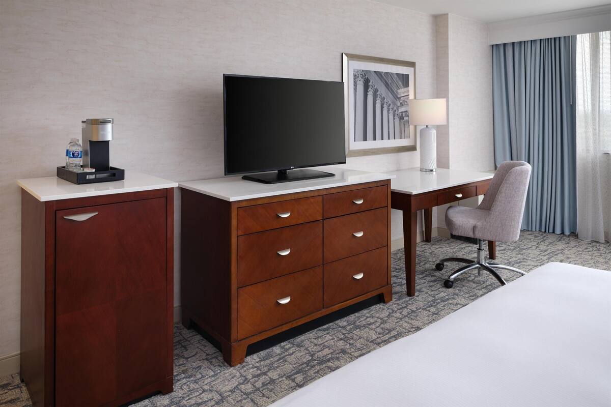Habitación de hotel con un armario de madera, un televisor de pantalla plana, un escritorio con lámpara, una silla y una cama.