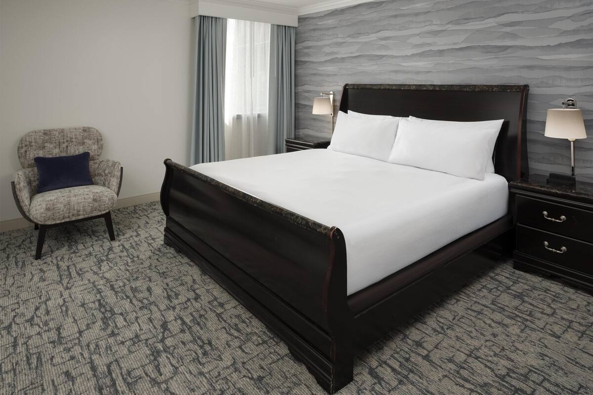 Una habitación de hotel con una cama grande, una silla, una mesita de noche y una lámpara.