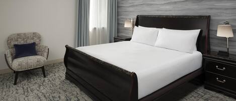 A hotel room with a large bed, a chair, a nightstand, and a lamp.