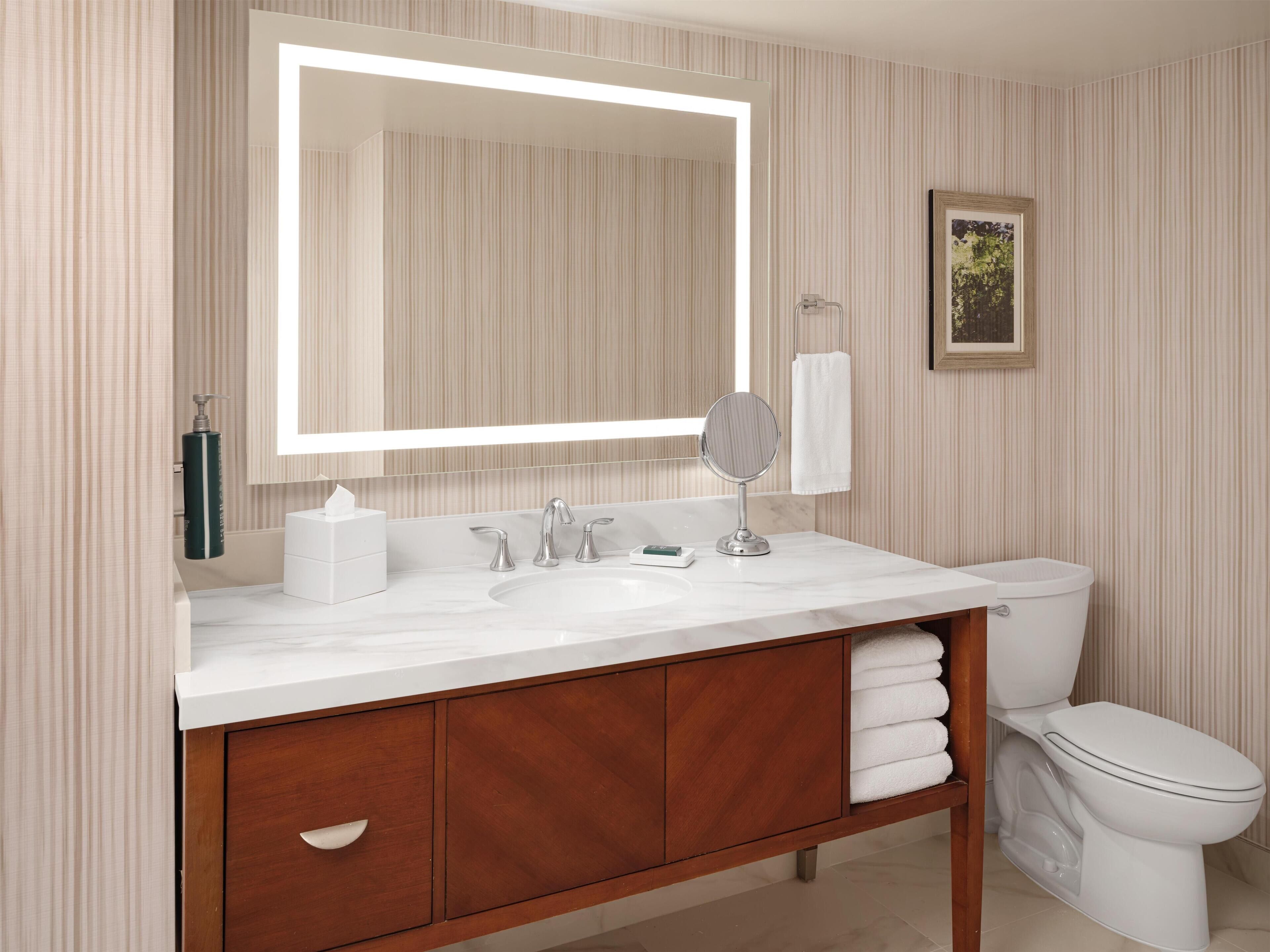 A bathroom with a large mirror, white sink, wooden vanity, and a toilet.