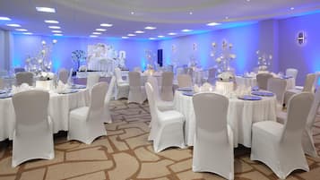 Un salón de banquetes con mesas redondas, sillas blancas y centros de mesa azules.