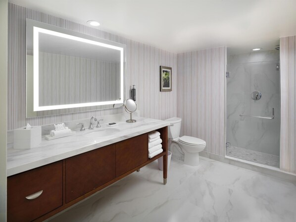 A modern bathroom with a large mirror, a vanity with a sink, a toilet, and a shower area.