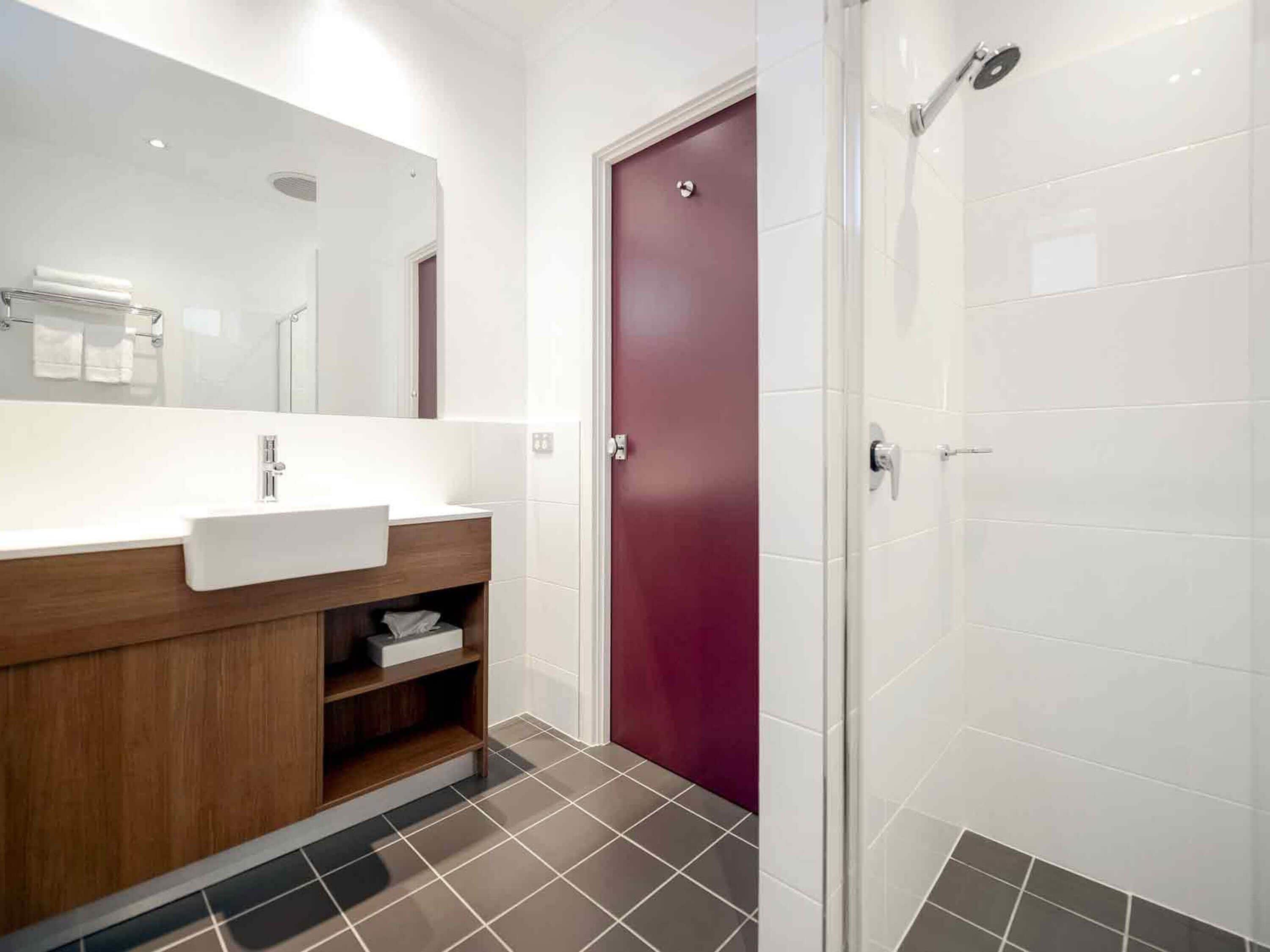 A modern bathroom with a large mirror, a sink, a vanity, a shower, and a door.