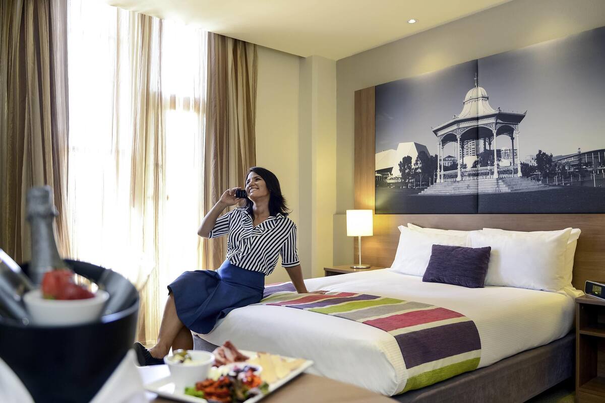 Habitación de hotel con cama, mesita de noche con lámpara, un plato de comida y un ventanal con cortinas.