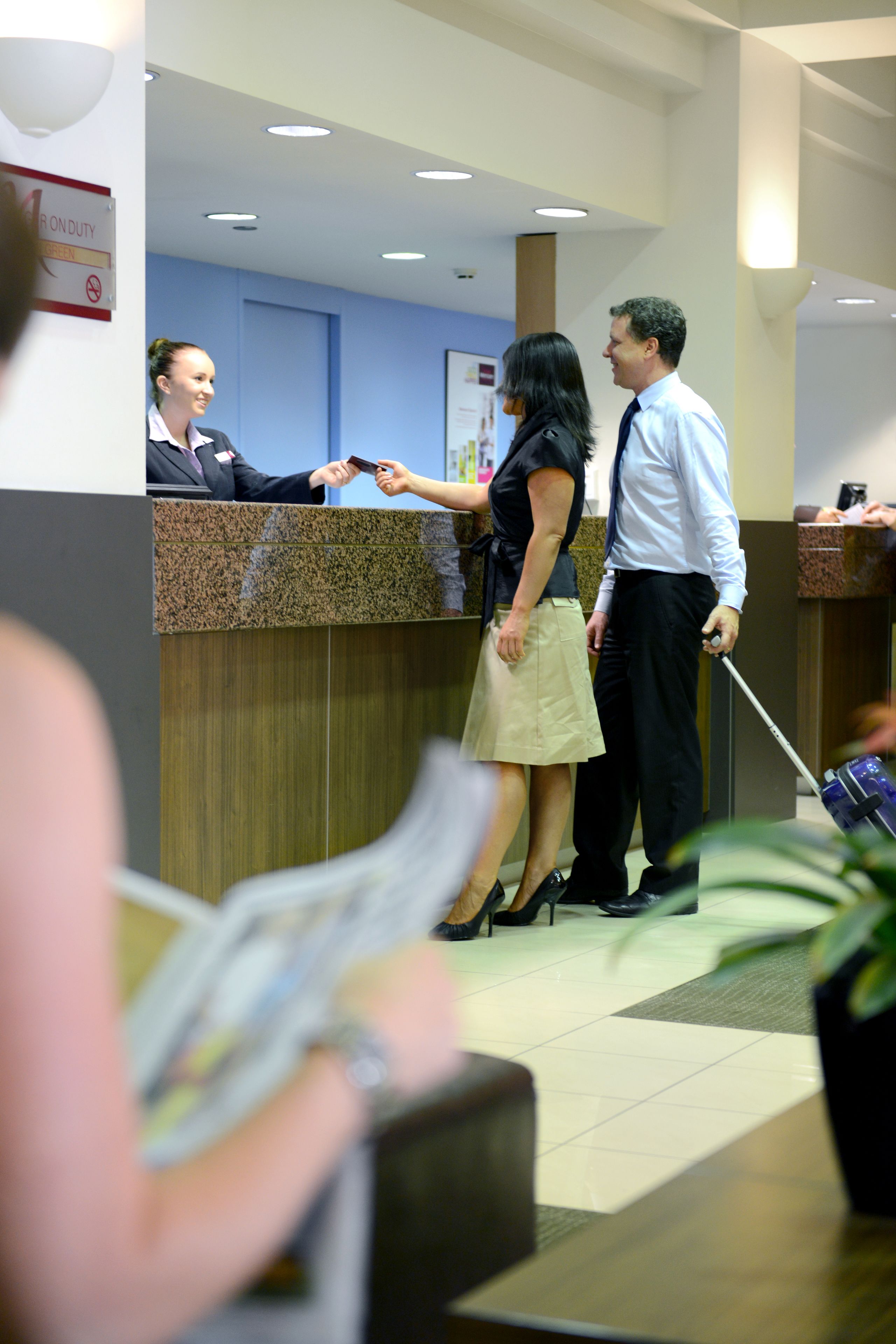 A reception area with a counter, a woman in a black top and beige skirt, and a man in a white shirt and black pants.