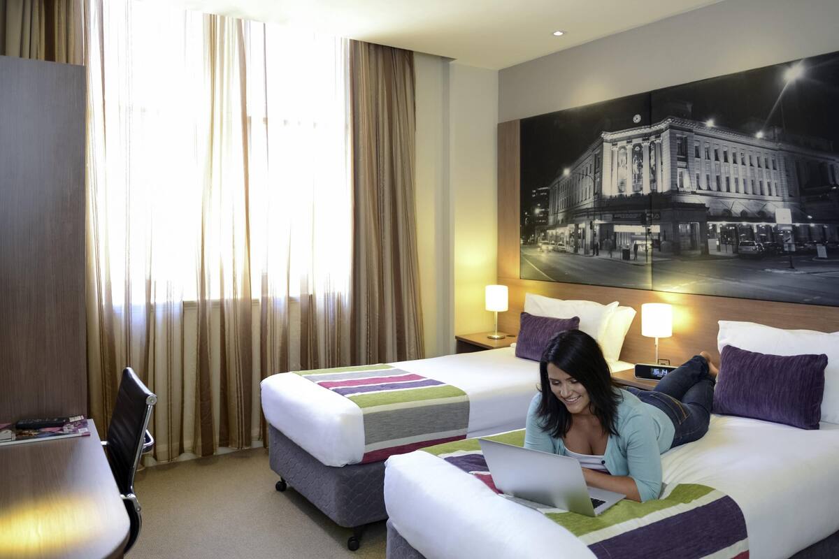 Habitación de hotel con dos camas, un escritorio y un ventanal con cortinas.