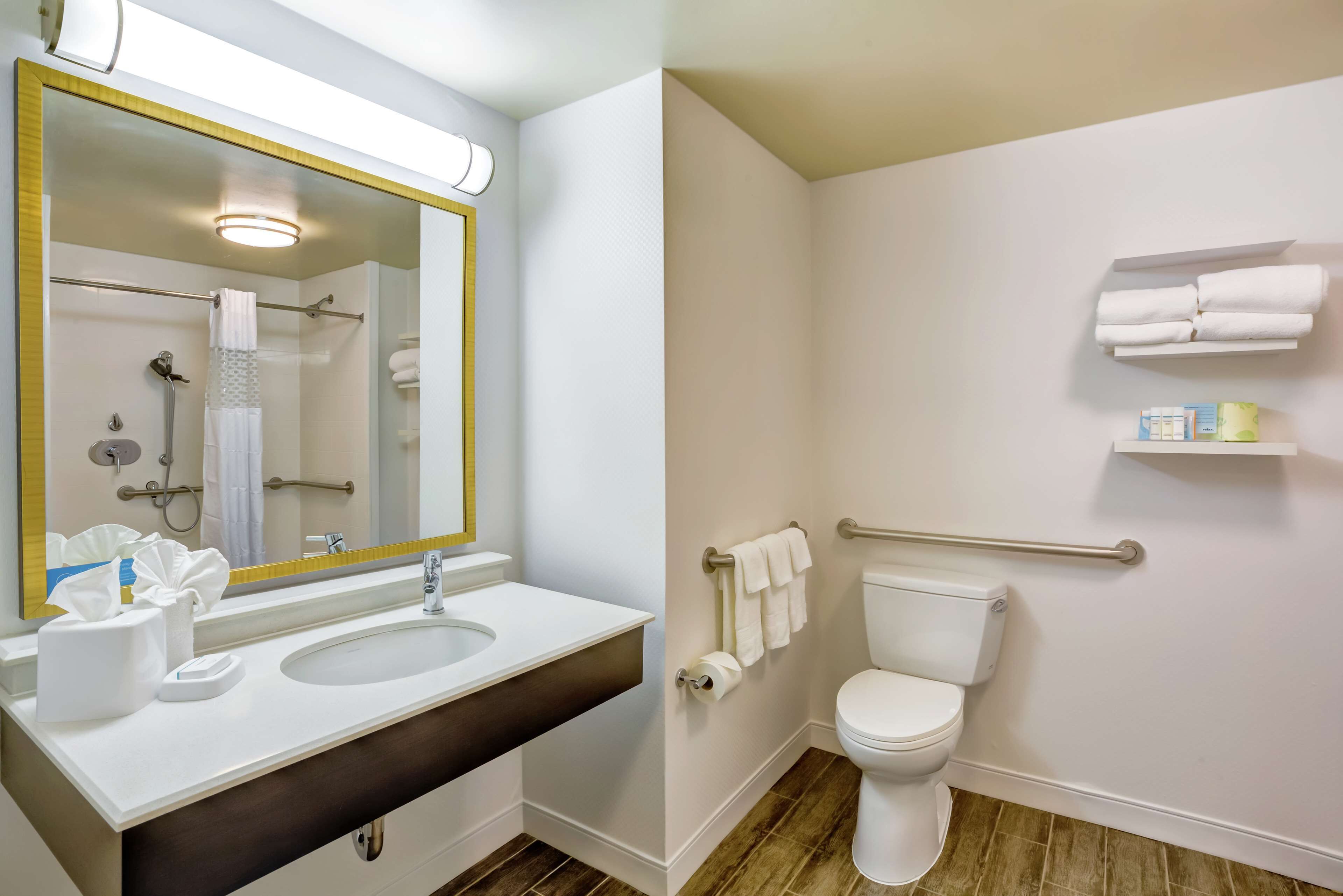 A bathroom with a white sink, mirror, and toilet. There are towels and toiletries on the wall.