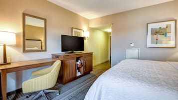 A hotel room with a bed, a desk with a chair, a television, and a cabinet.