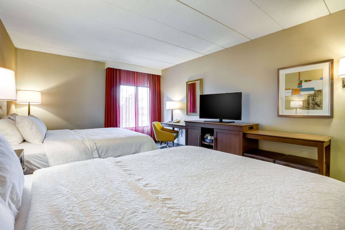 A hotel room with two beds, a desk with a television, a chair, and a desk lamp.