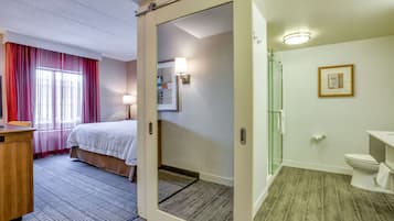A hotel room with a bed, a desk, a shower area, and a bathroom.