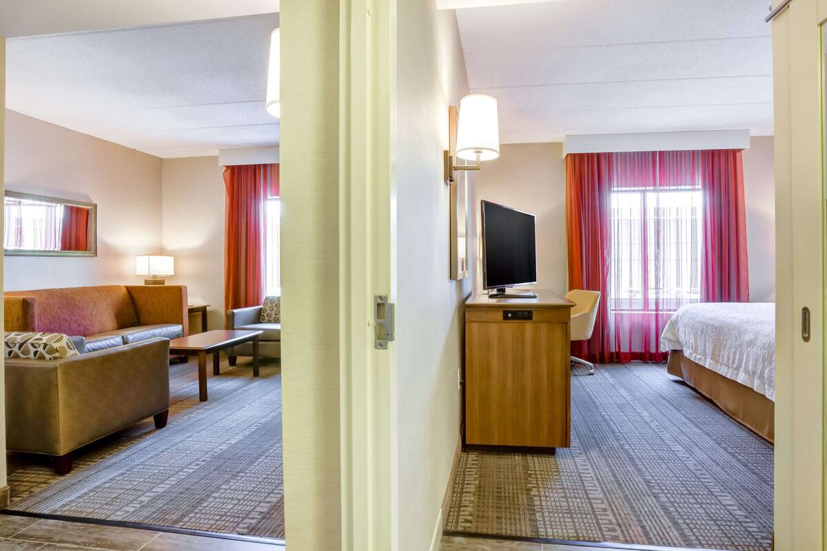 A hotel room with a sofa, a desk, a TV, a bed, and a window with curtains.