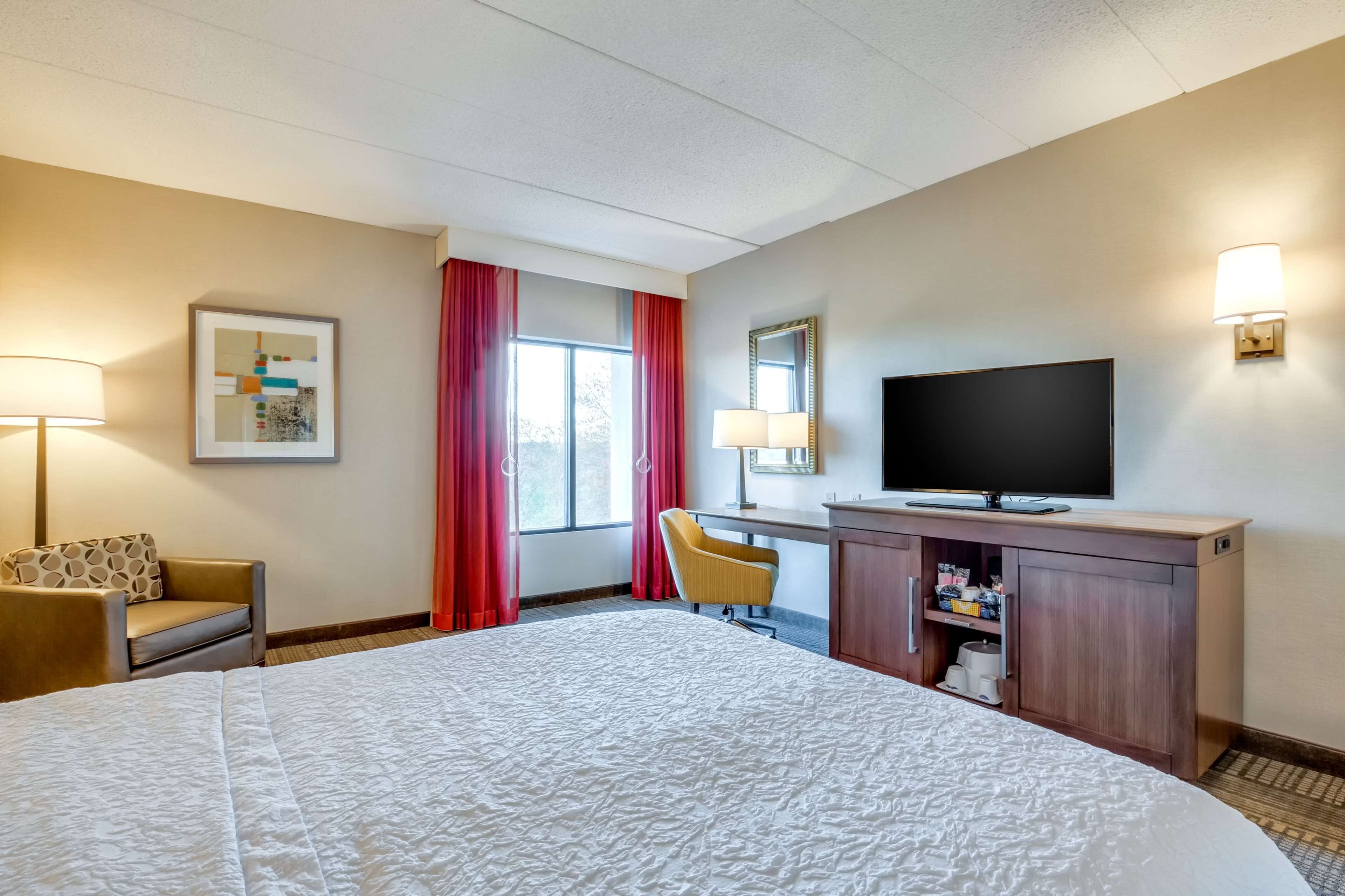 Una habitación de hotel con una cama grande, un escritorio con televisor, una silla y una lámpara de escritorio.
