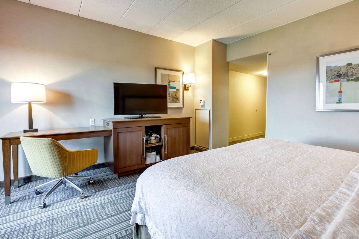 A hotel room with a bed, desk, chair, television, and artwork on the walls.