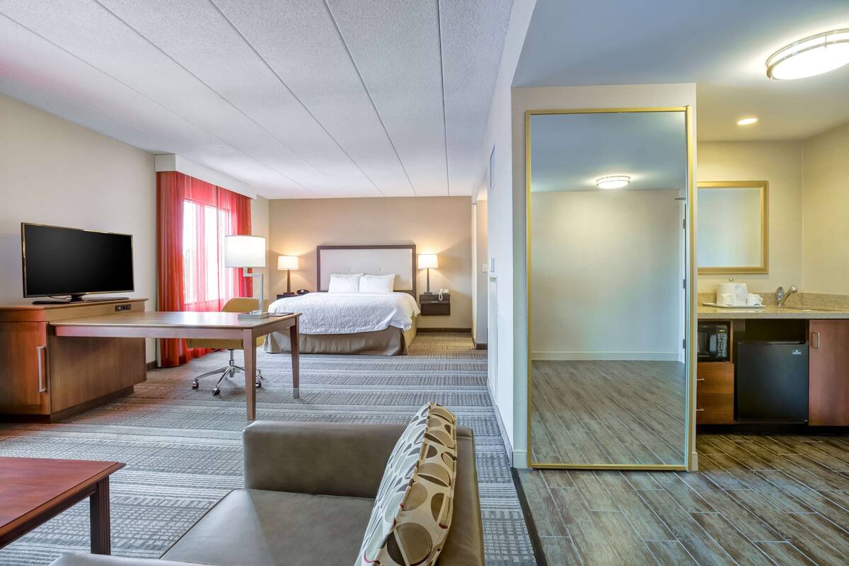 A hotel room with a bed, desk, TV, and a mirror.