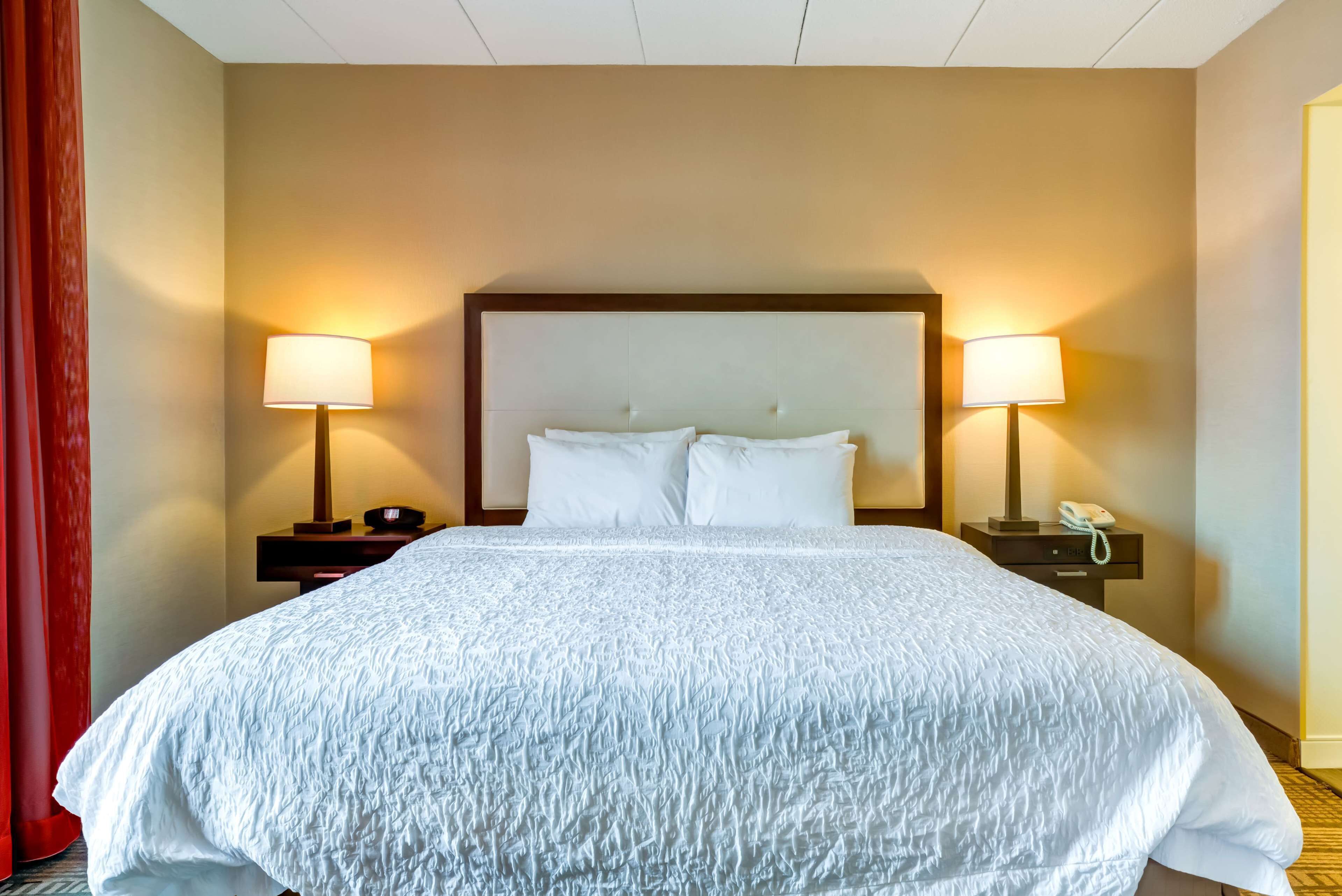 A hotel room with a large bed, two bedside tables with lamps, and a red curtain.