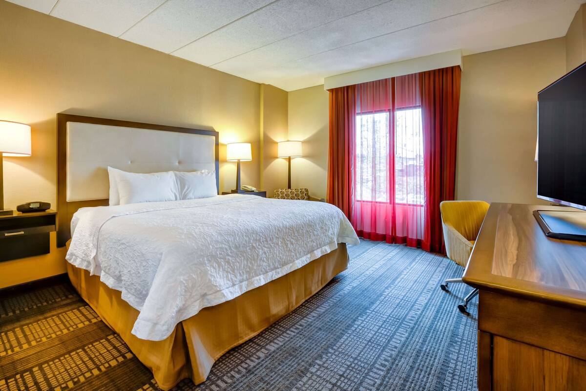 A hotel room with a large bed, two bedside tables with lamps, a desk with a chair, and a TV.