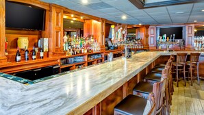 A bar area with a long counter, multiple seating options, and a variety of bottles and glasses. - Hampton Inn Boston - Norwood (Norwood)