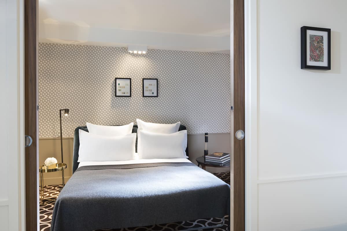 A hotel room with a bed, a nightstand, a lamp, and two framed pictures on the wall.