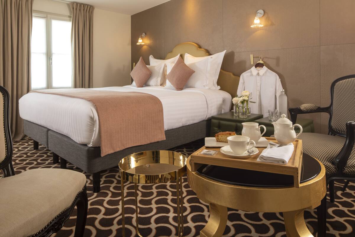 A hotel room with a large bed, bedside table with tea set, and a chair.