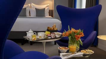 Een hotelkamer met een bed, een ontbijfwagen met eten en drinken, een stoel en een vaas met bloemen.