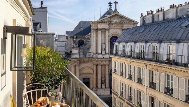 Varanda com mesa posta para o pequeno-almoço, com vista para um edifício histórico com cúpula e estátuas.
