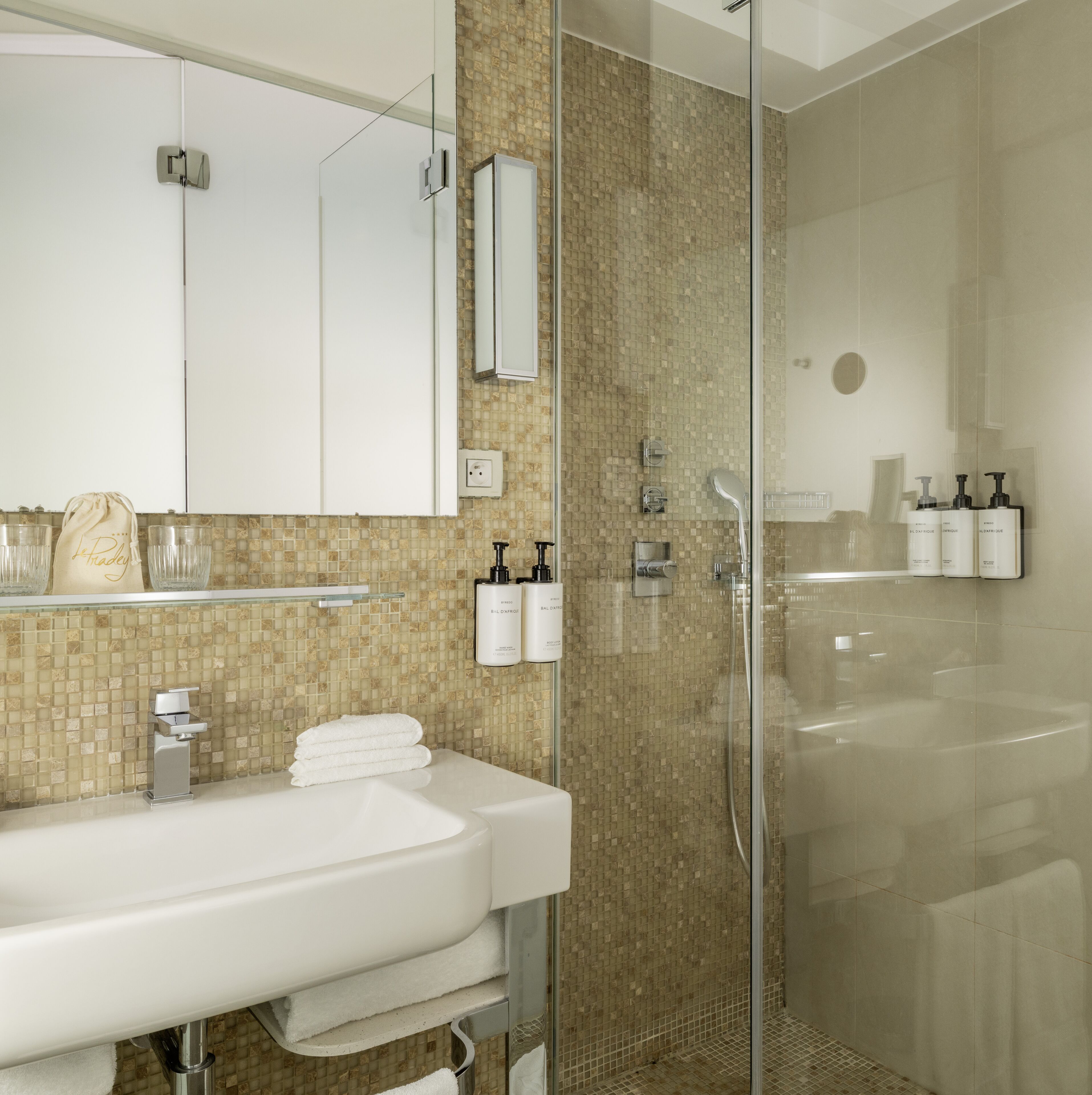 Un baño moderno con ducha envuelta en vidrio, lavamanos blanco y artículos de aseo colgados en la pared.