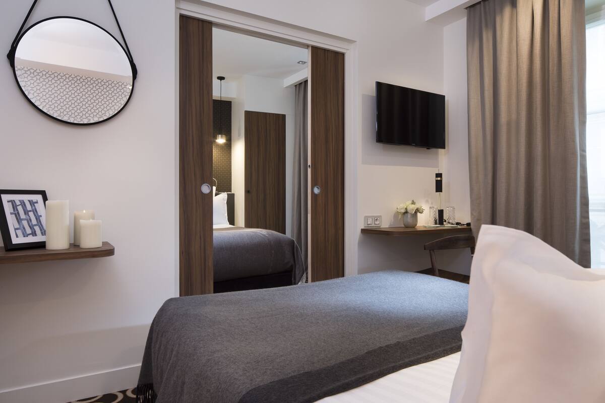 A hotel room with a bed, a bedside table, a TV, a mirror, and a door leading to another room.