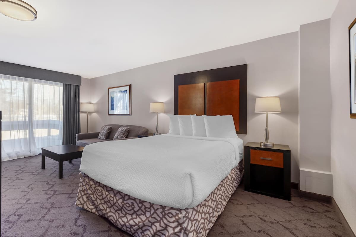 Ein Hotelzimmer mit einem großen Bett, einer Sitzecke, einem kleinen Tisch, zwei Nachttischlampen und einem gerahmten Bild an der Wand.
