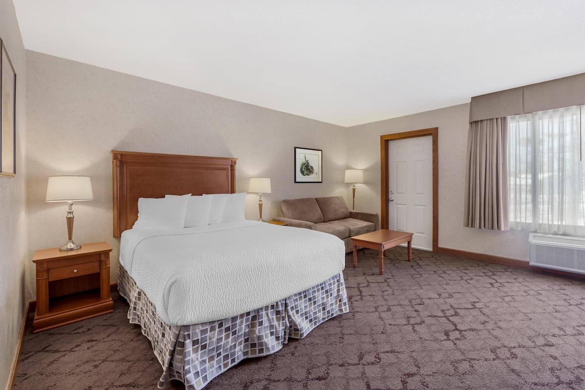 Ein Hotelzimmer mit einem großen Bett, zwei Nachttischen mit Lampen, einem Sofa, einem kleinen Tisch und einem Fenster mit Vorhängen.
