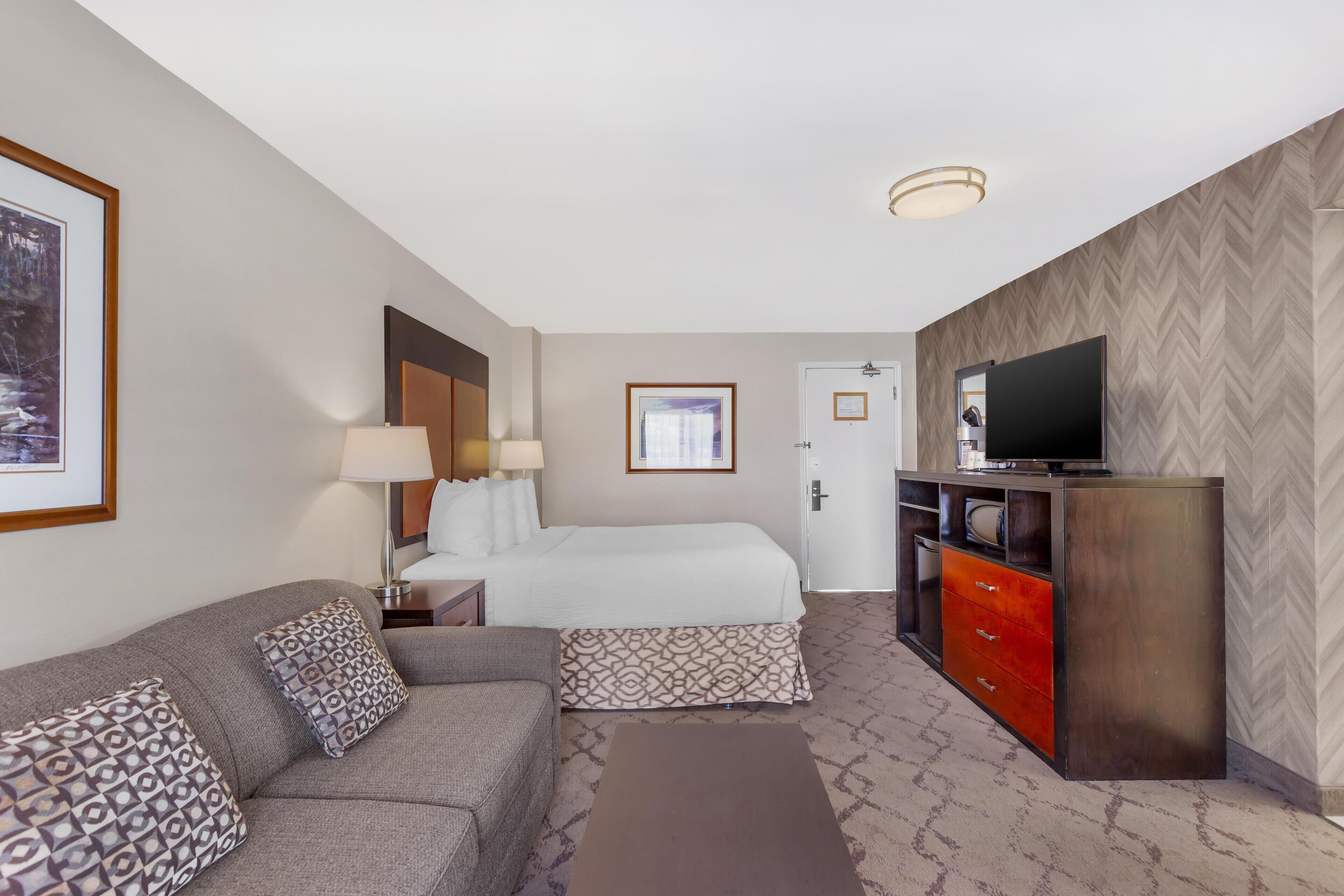 A hotel room with a bed, a sofa, a TV, and a dresser.