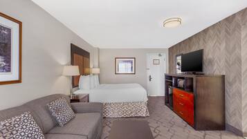 Quarto de hotel com cama, sofá, televisão e cômoda.