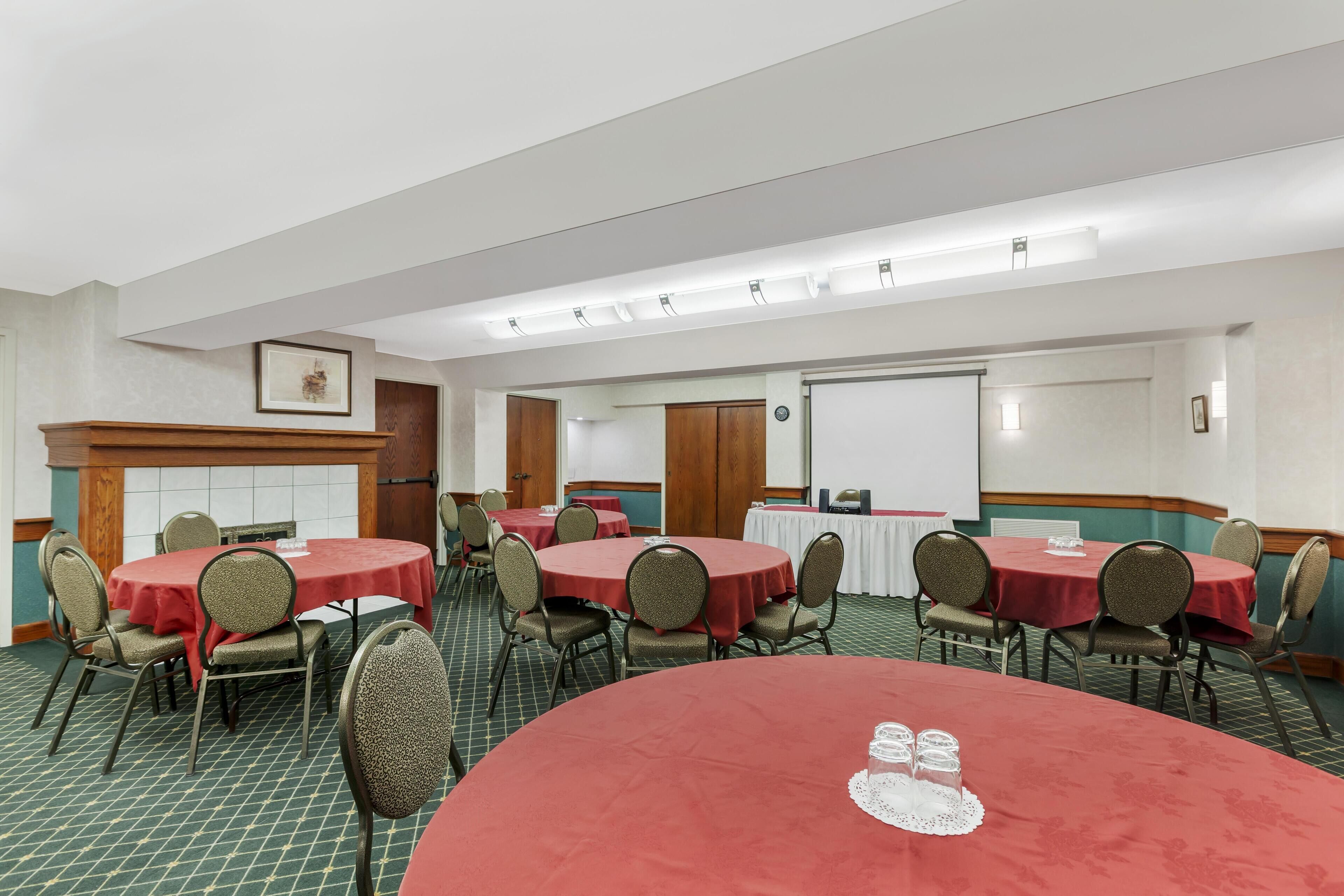 A conference room with round tables and chairs, a whiteboard, and a projector screen.