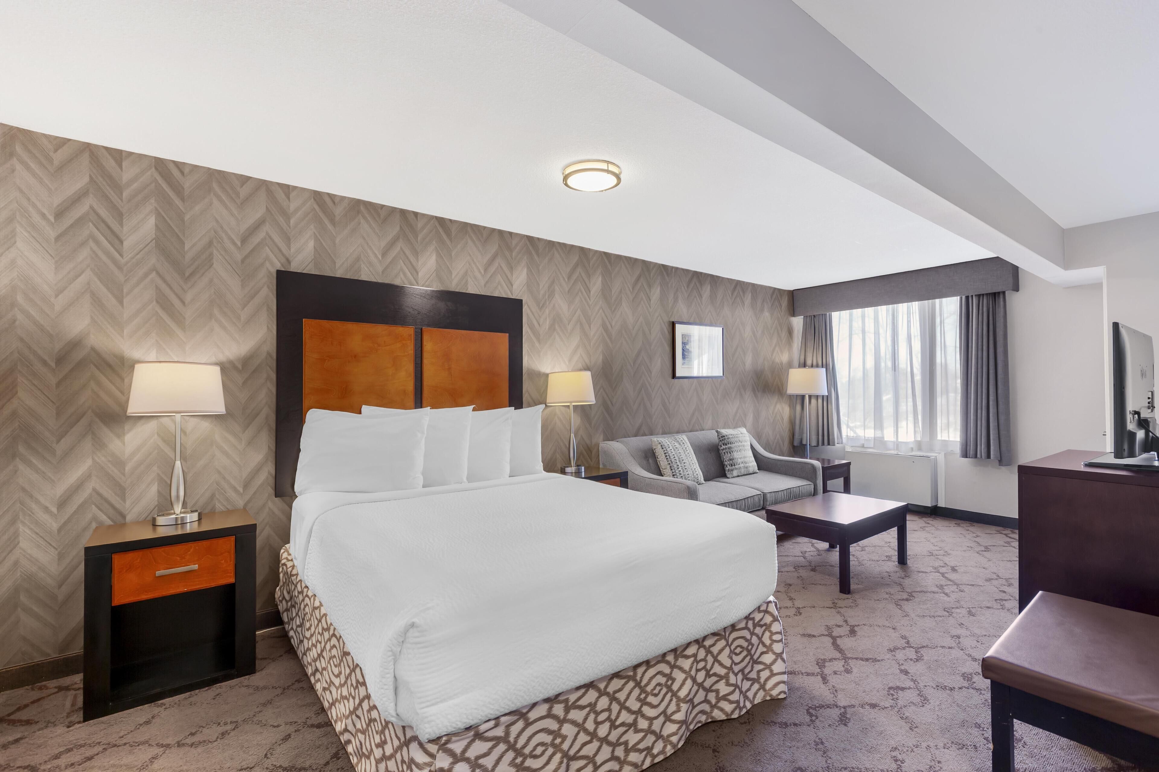 Quarto de hotel com uma cama grande, duas mesas de cabeceira com luminárias, um sofá, uma mesa de centro e uma televisão.