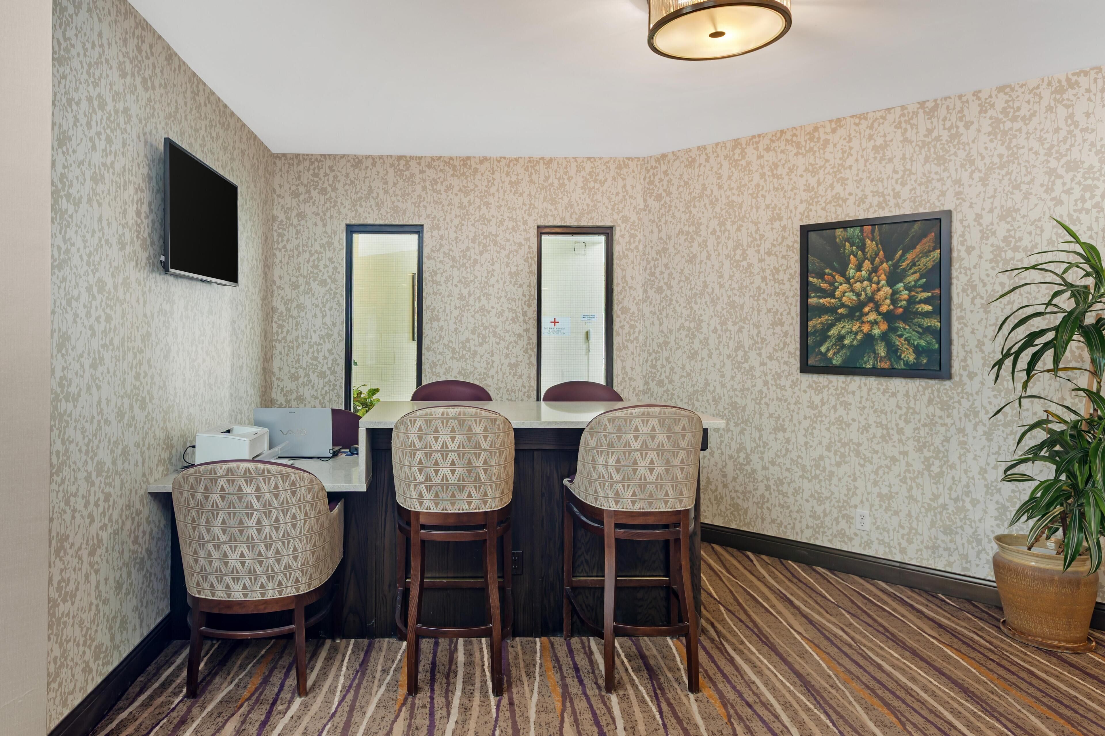 A room with a dining table, two chairs, a TV mounted on the wall, and a potted plant.