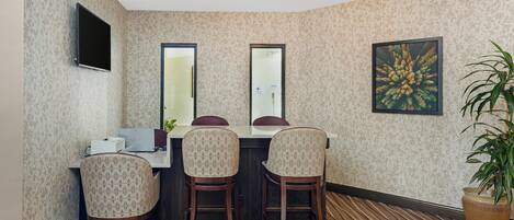 Una habitación con una mesa de comedor, dos sillas, un televisor montado en la pared y una planta en maceta.